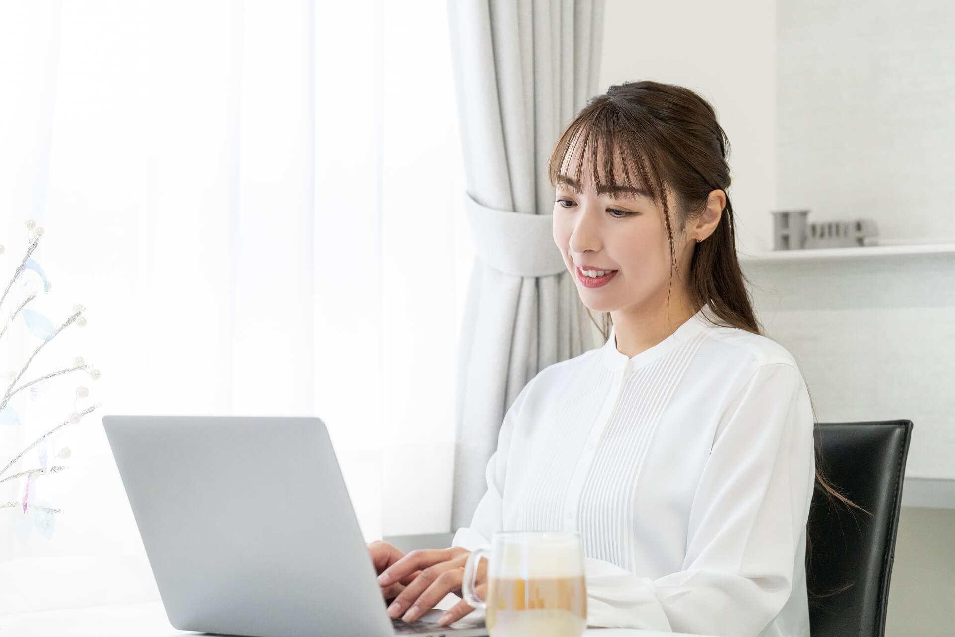 パソコンの前で笑顔を浮かべている女性の画像